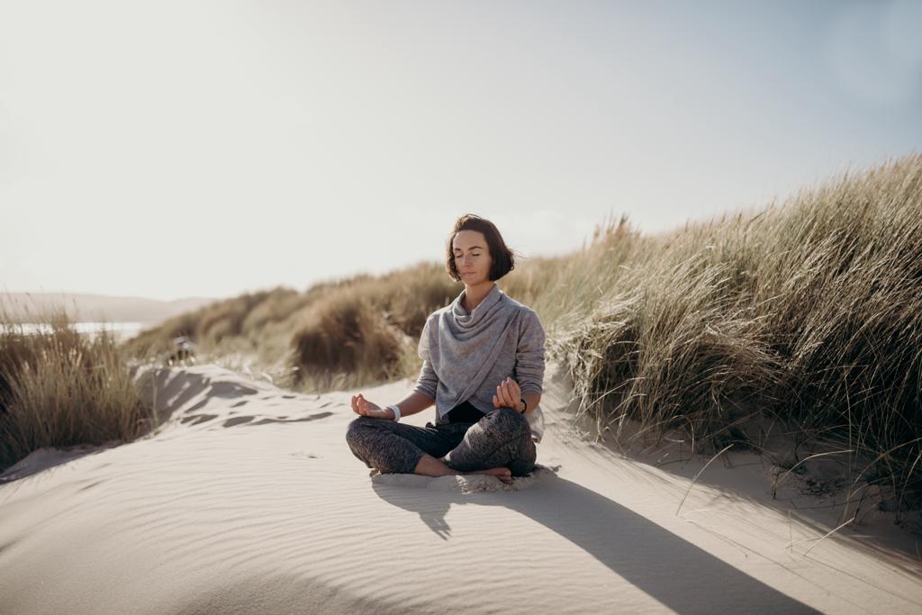 Yoga teacher sitting on sand dunes meditating in the sun.