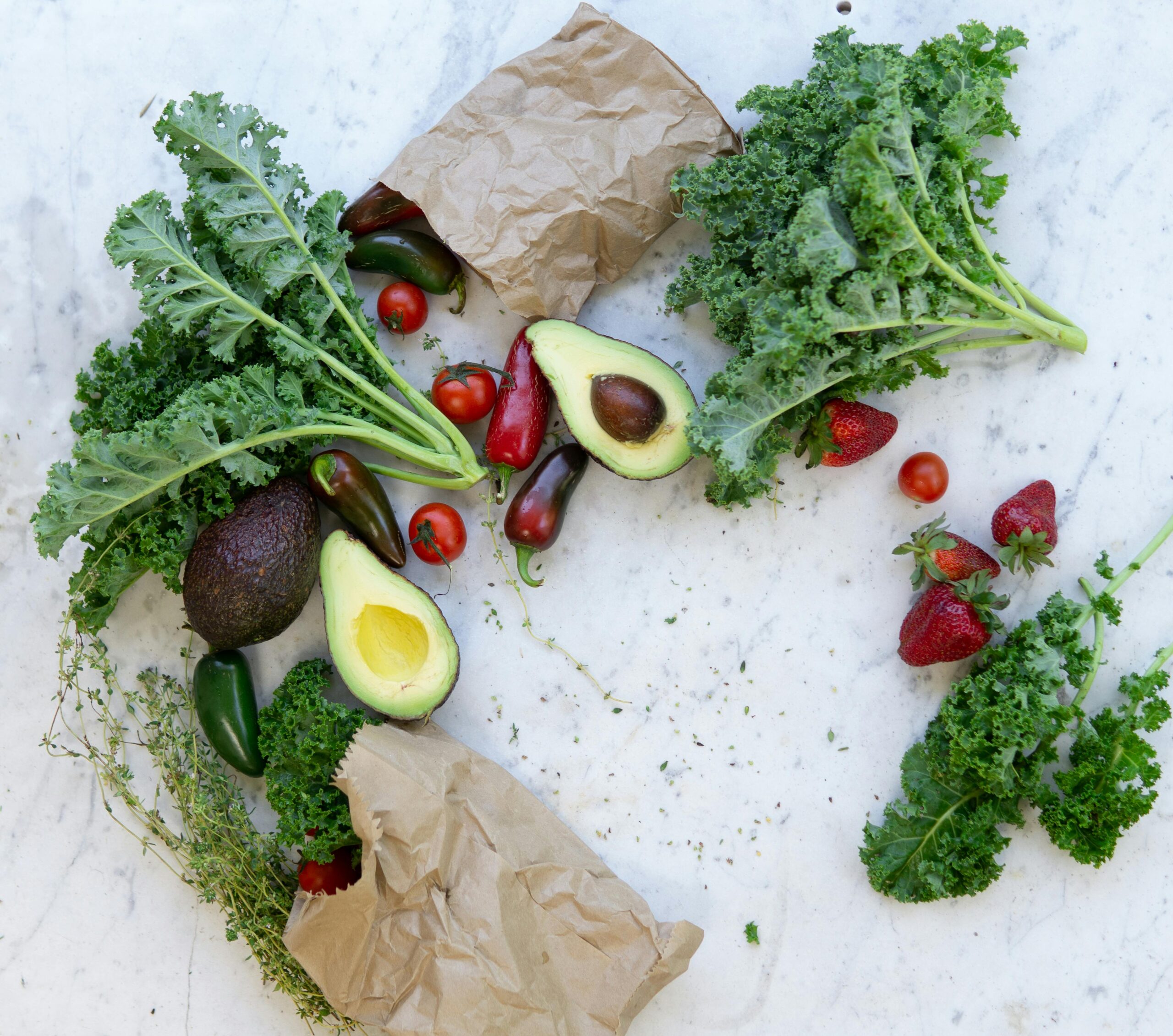 Avocados, strawberries, tomatoes, kale and chillies spread on a surface to show an ancient approach to modern health.