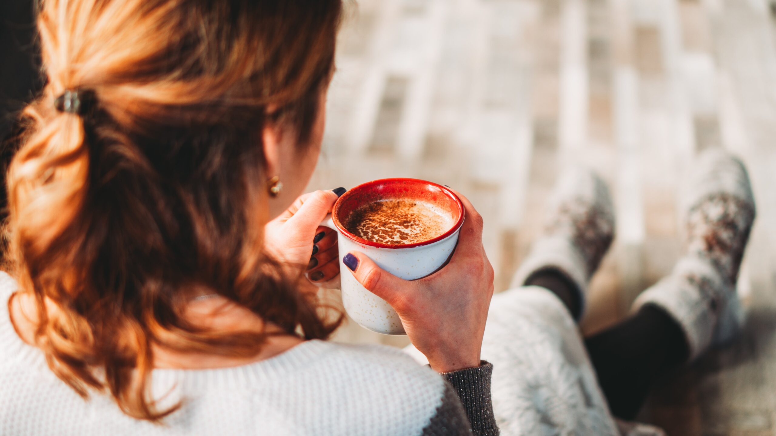 A woman looking cosy and holding a hot drink.