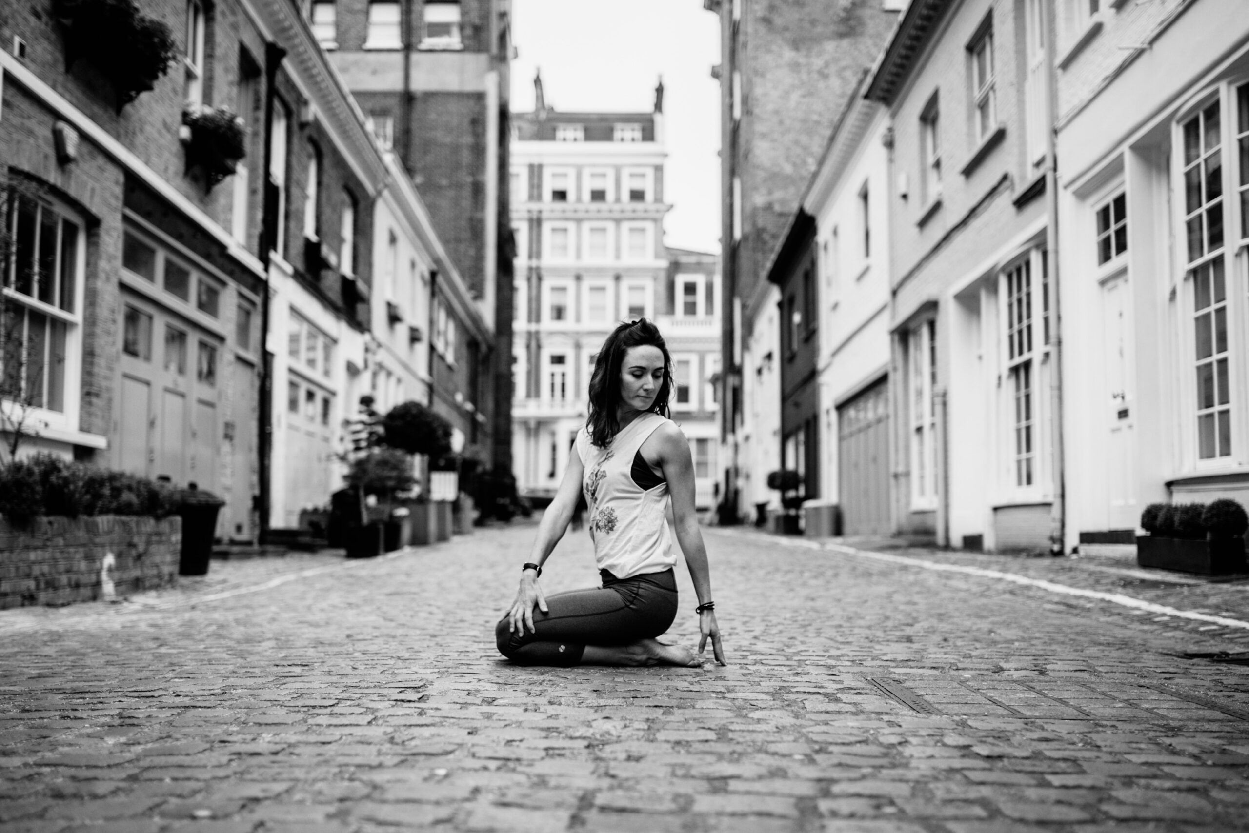 Yoga teacher Anney in a seated twist on a cobbled street to represent yoga and me, her personal journey.