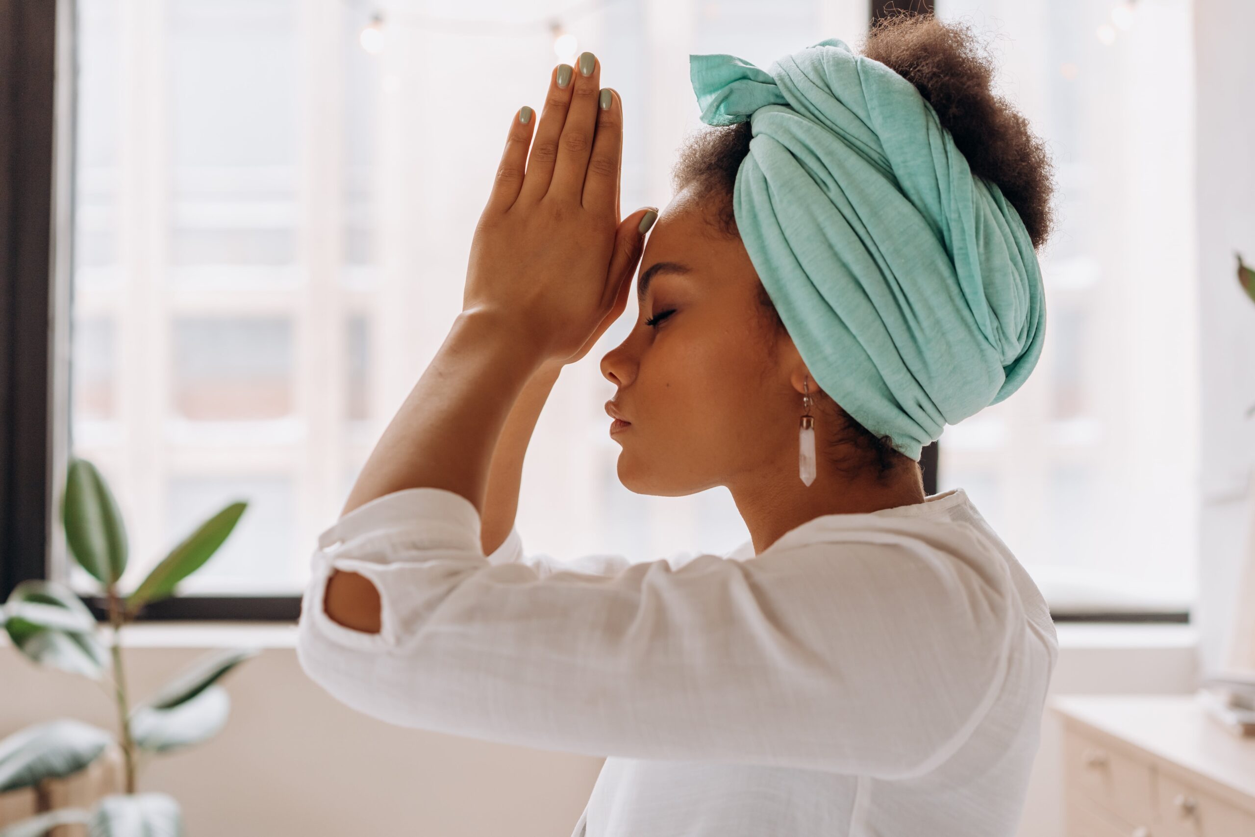A side view of a woman with her hands in a prayer mudra at her third eye to signify connecting to and following her intuition.